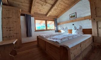 A cozy bedroom with a wooden ceiling and oak wardrobes. The window offers a view of nature.