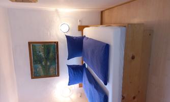 A cozy bedroom with a double bed and blue cushions. A green picture hangs on the wall, and there is soft lighting.