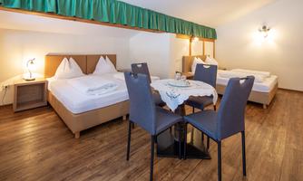 A cozy room with two beds and a dining table. The wooden floor creates a warm atmosphere.