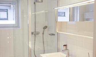 A modern bathroom with a glass shower and a stylish vanity unit. The walls are bright and shiny, creating a clean impression.