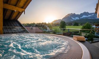 A hot tub with bubbling water on a terrace. In the background, mountains and a beautiful sunset can be seen.