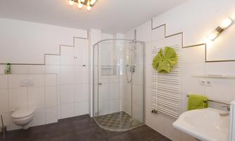 A modern bathroom with a walk-in shower and light tiles. The decor is tidy and in soft colors.
