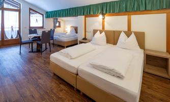 A cozy hotel room with two single beds and a warm wood look. There is a small table with chairs and plenty of natural light from the windows.