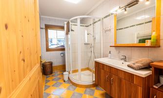 A modern bathroom with a shower and a wooden sink. The floor is tiled with colorful tiles and there is a window that brings in natural light.