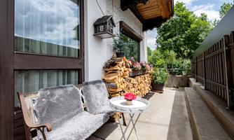 A cozy balcony with a stack of wood, a small table, and a bench. Green plants and a beautiful view of nature enhance the relaxed atmosphere.