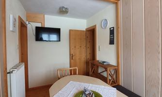 An inviting interior with a table, chairs, and a television on the wall. The walls are partially made of wood, creating a cozy atmosphere.