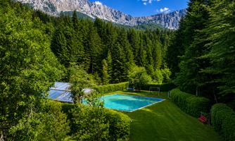A picturesque landscape with a clear swimming pool in the center. In the background, majestic mountains rise and dense forests.