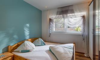 A cozy bedroom with a wooden bed and light wooden floor. Bright walls and large windows create a friendly atmosphere.