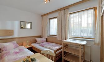 A cozy room with two beds and plenty of natural light. The walls are bright, and the furniture is made of wood.