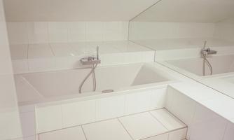 A modern bathroom with a white bathtub and large mirrors. The tiles are also in white, giving a clean and elegant impression.