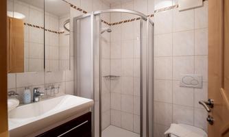 A modern bathroom with a shower cubicle and a sink. The walls are tiled and the design is bright and inviting.