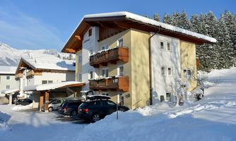 A cozy house in the snow with multiple balconies. Surrounded by snow-covered trees and mountains.