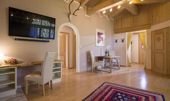 A bright room with a wooden ceiling and a TV on the wall. There is a table, chairs, and a rug in the room.