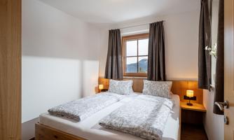 A bright bedroom with two single beds and a large window front. The rooms are cozy, designed with wood and soft colors.