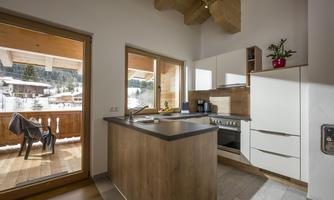 A modern kitchen with wooden details and large windows that offer a view of the winter landscape. The room is bright and friendly designed.