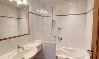 A modern bathroom with a bathtub and shower. Bright tiles and a large mirror create a friendly atmosphere.