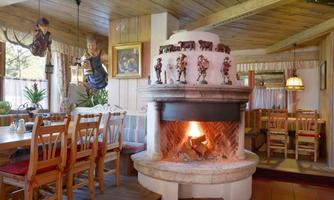 A cozy restaurant with wood decor and an open fireplace. In the background, tables and chairs as well as decorative figures are visible.