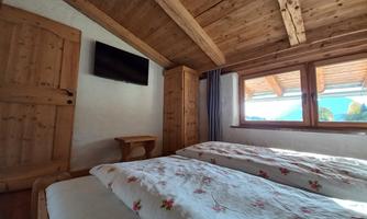 A cozy bedroom with two beds and wooden ceilings. Large windows let in plenty of light and provide a view outside.