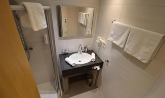 A modern bathroom with a shower, sink, and mirror. Two towels are hanging decoratively on the wall.