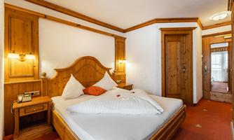 A cozy bedroom with a large double bed and wooden paneling. The walls are light, and there are warm light sources for an inviting atmosphere.