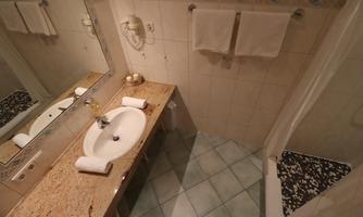 A bathroom with a sink, towels, and a shower. The floor is tiled and the walls are light.