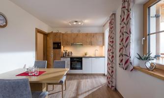 A modern kitchen with a dining table and chairs. Bright walls and large windows create a friendly atmosphere.