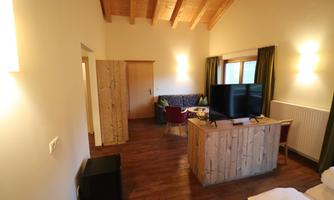 A cozy room with wood paneling and a television. The room features a seating area and large windows for natural light.
