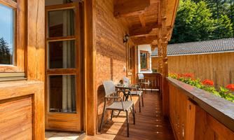 A cozy wooden balcony with chairs and a beautiful view of nature. The sunny atmosphere creates an inviting and relaxing environment.