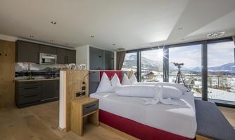 A modern room with a large bed and a stylish kitchen.  
Large windows offer a beautiful view of the mountains and the landscape.