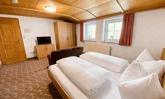 A cozy room with wooden elements and a large bed. There is a television and windows with curtains.