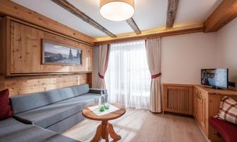 A cozy living room with a gray couch and a round wooden table. Large windows let in plenty of daylight, and the wood decor gives a warm atmosphere.