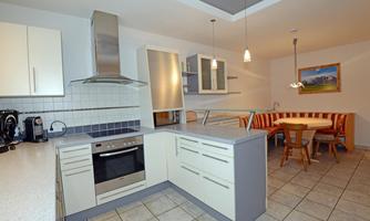 A modern kitchen with bright cabinets and an elegant stove. In the background, there is a cozy dining area with a round table and chairs.