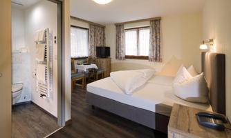 A cozy hotel room with two beds, a seating area, and a bathroom. The room is bright and cheerfully decorated.