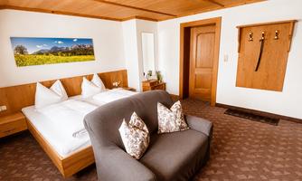 A cozy room with a double bed and a bright sofa.  
On the wall, there is a picture of a landscape, and there is a wardrobe near the door.