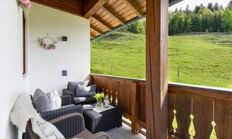 A cozy balcony with two sofas and a table. In the background, a green meadow and trees are visible.