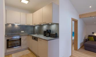 A modern kitchen with bright cabinets and a stainless steel sink. The floor is made of wood and there is a cozy seating area in the background.