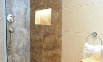 A modern bathroom with a glass shower area and elegant tiles. Fresh towels are ready on the wooden shelf.