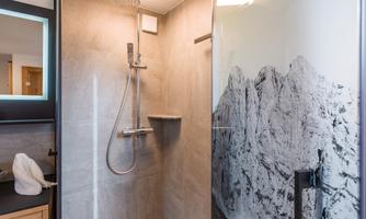 A modern shower with gray tiles and a clear glass partition. In the background, there is a large mountain motif depicted.