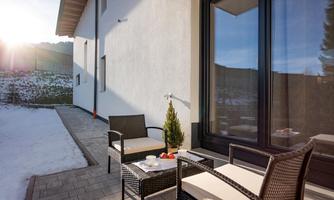 A cozy terrace with modern garden furniture and a beautiful view. The sun is shining on the snow-covered ground.