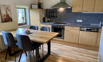 A modern kitchen with wooden cabinets and a large dining table. The room is bright and welcoming with a window that lets in natural light.