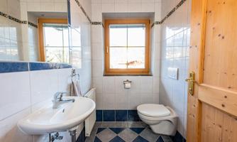 A modern bathroom with bright tiles and a window. It features a sink and a toilet.