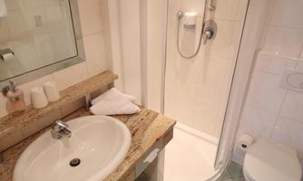 A bright bathroom with a shower, a sink, and a toilet. The walls are tiled, and the floor is in a soft green tone.