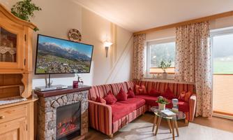 A cozy living room with a red sofa and television. Large windows let in a lot of light and provide a view outside.