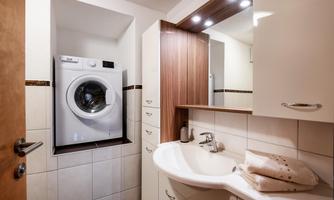 A modern bathroom with a washing machine in a built-in cabinet. The room is bright and well-organized, featuring a sink and towels.