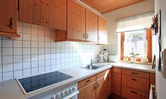 A bright kitchen with wooden cabinets and white walls. The countertop is equipped with a stove and a sink.