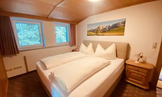 A cozy bedroom with a double bed and two windows. A picture of a mountain landscape is hanging on the wall.