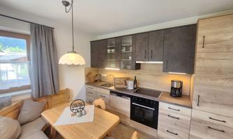 A modern kitchen with wooden cabinets and a cozy dining area. The room is bright and inviting, with a window view of the surroundings.