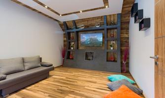 A modern living room with a gray sofa and colorful cushions on the floor. The walls are decorated with wood paneling and decorative shelves.