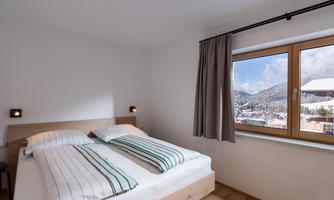 A cozy bedroom with a double bed and modern comforters. Large windows offer a view of the snow-covered mountains.