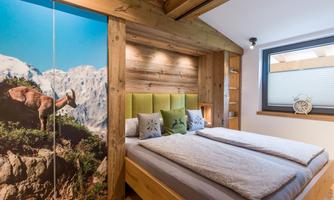 A modern bedroom with wooden elements and a large bed. On the wall, there is a picture of a mountain landscape with a chamois.